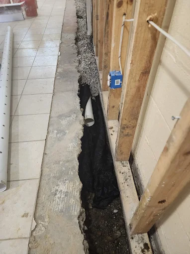 Interior basement French drain trench along wall.