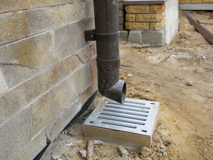 French drain catch basin connected to downspout beside home foundation